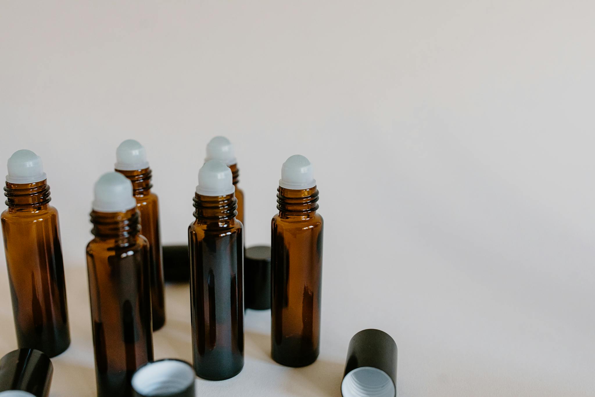 Set of amber glass roller bottles for essential oils on a neutral backdrop.